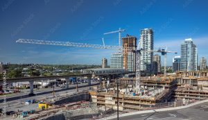 A large construction site in San Francisco County features multiple cranes working on high-rise structures. In the background, several completed skyscrapers and a metro line blend seamlessly with the cityscape under a clear blue sky, all under the vigilant watch of Construction Security San Francisco County.